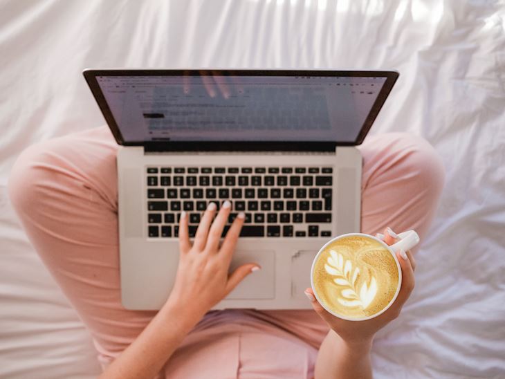 A person with laptop on their lap and a cup of coffee in one hand