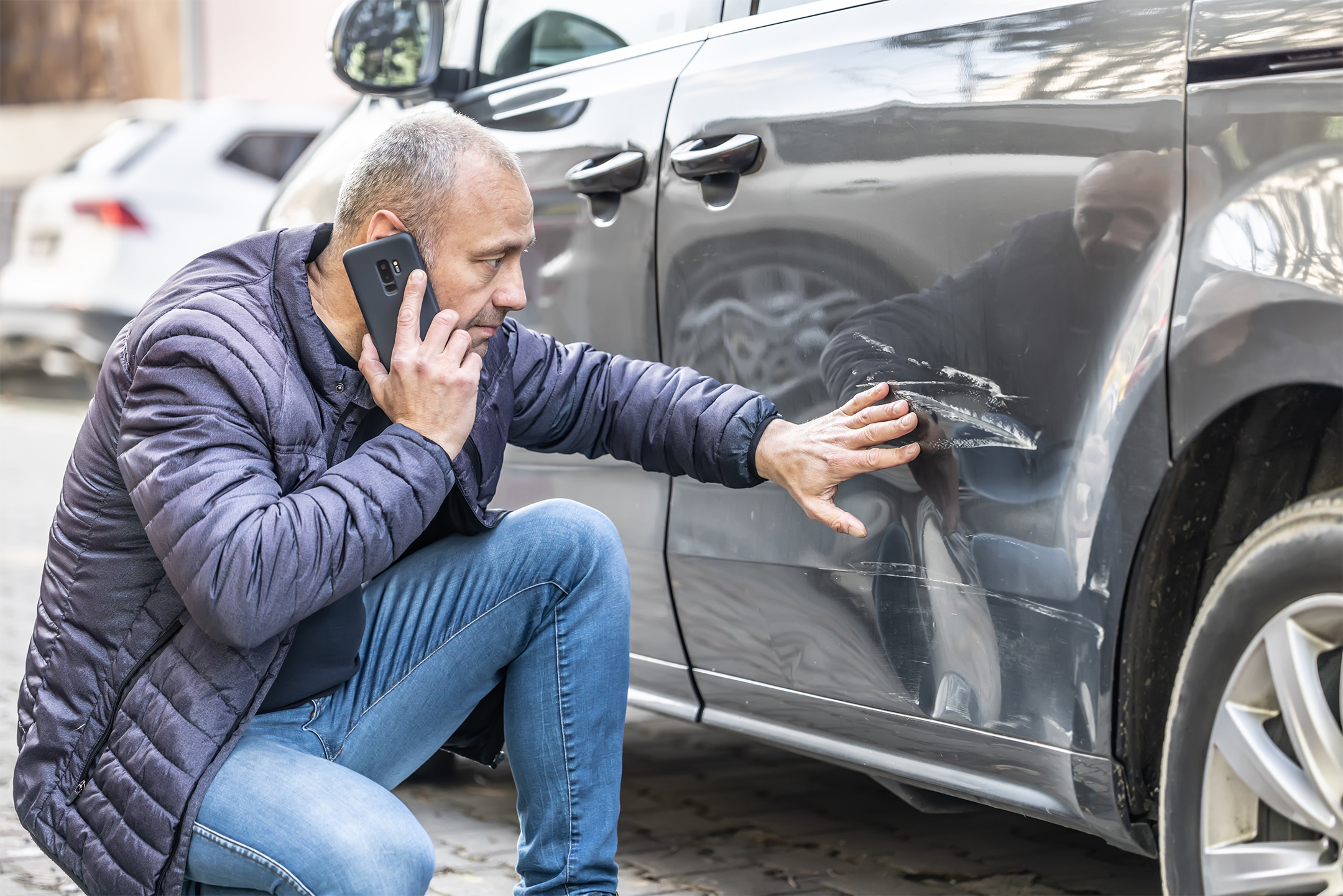 A man on the phone inspecting a dent in his car