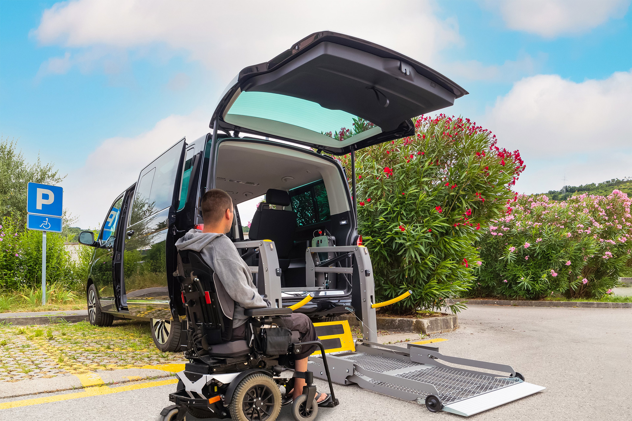 A man in a wheelchare next to a WAV with a rear lift