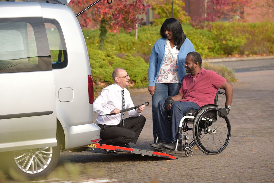 A supplier crouches by a WAV rear ramp and talks to two people