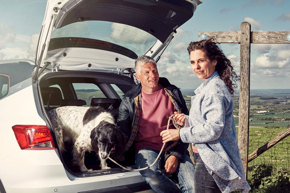 A couple standing by a car, with their dog in the boot