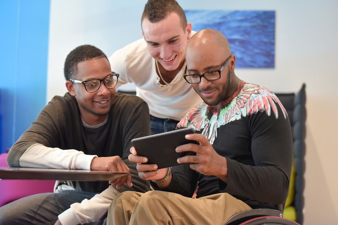 Three men smiling and looking at a tablet