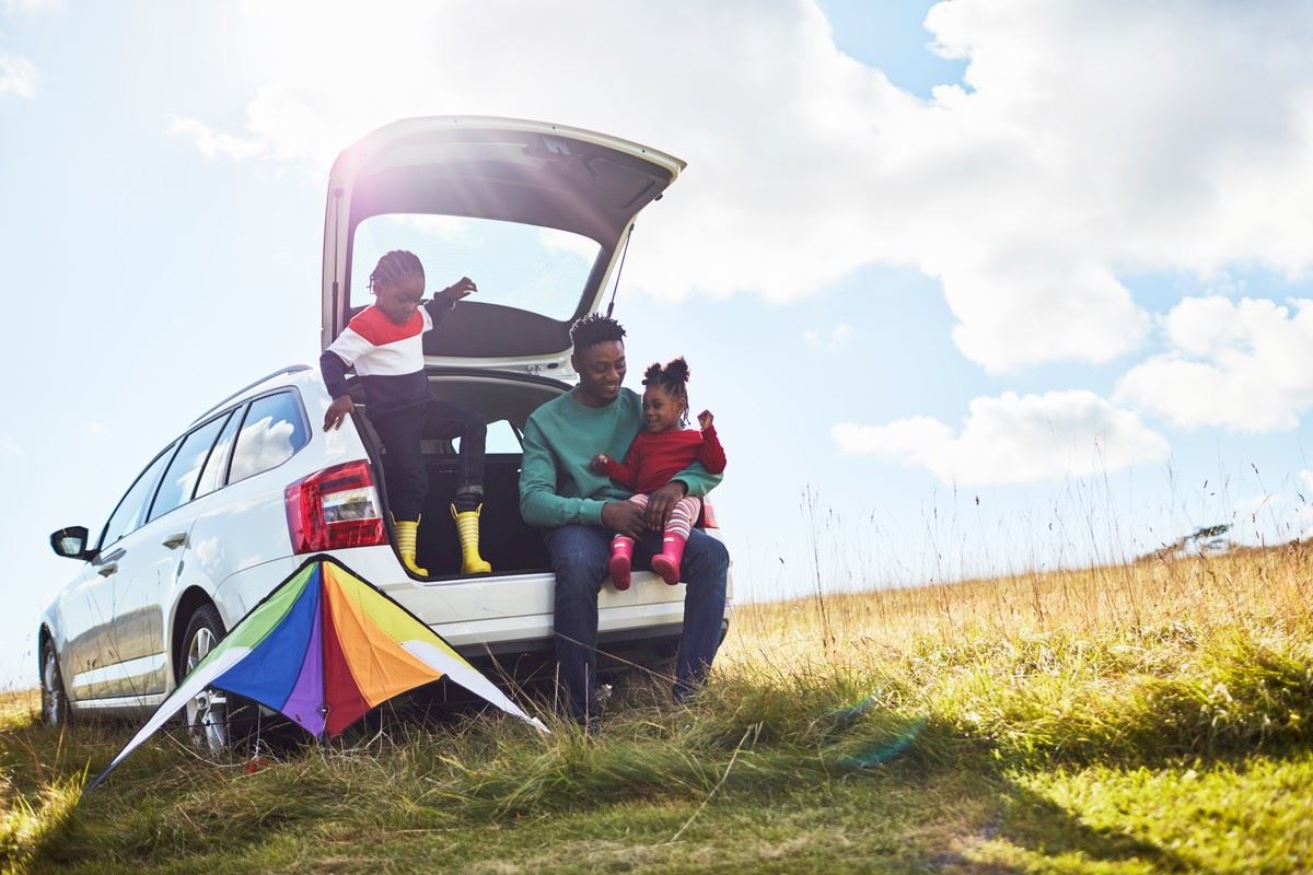 A family sitting in a car boot with a kite next to them