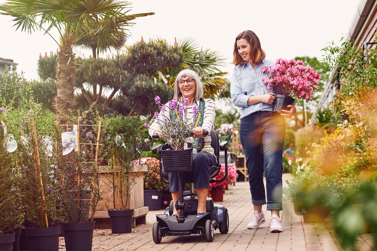 A woman shopping for plants on a mobility scooter, while talking to another woman