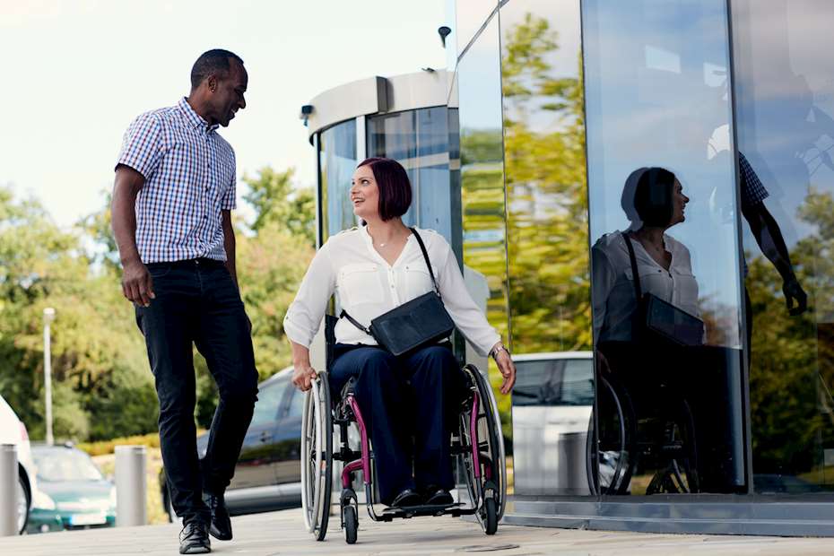 A man talking to a woman in a wheelchair outside an office building
