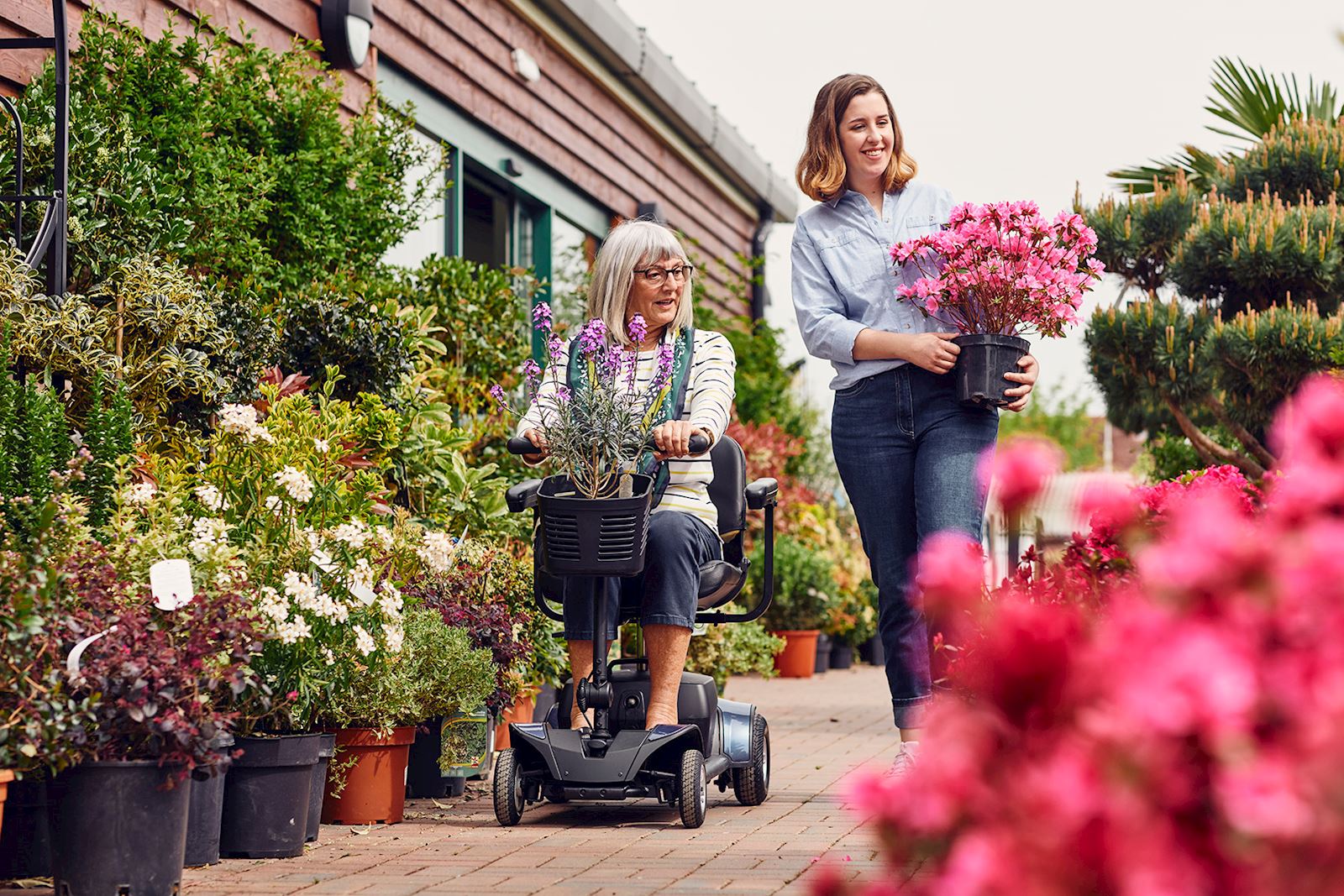 A lady riding a scooter alongside another lady carrying flowers