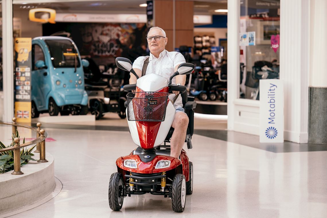 A man riding a red mobility scooter near a showroom