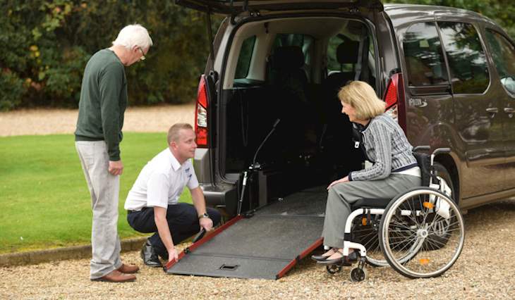 A supplier shows two people how a rear ramp on a WAV works