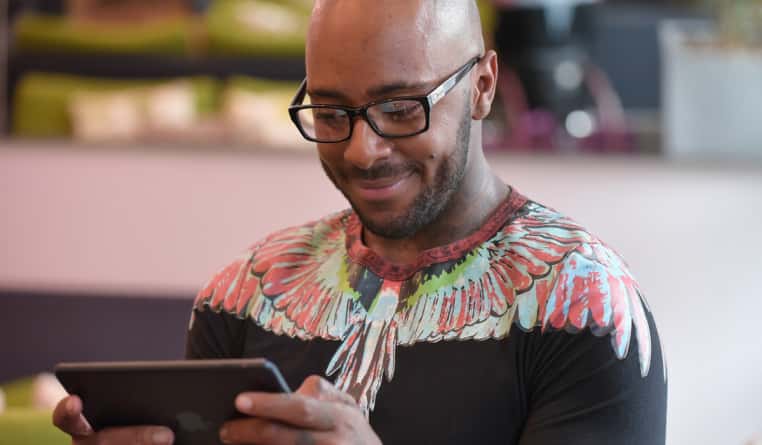 A man smiling while holding and looking at a tablet