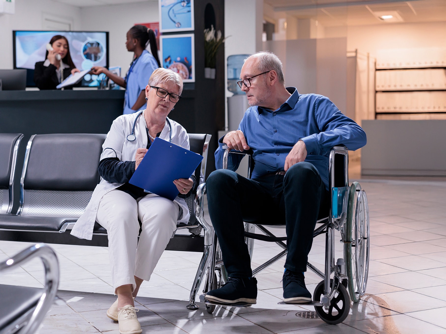 Female doctor with male patient in wheelchair in modern hospital waiting area.