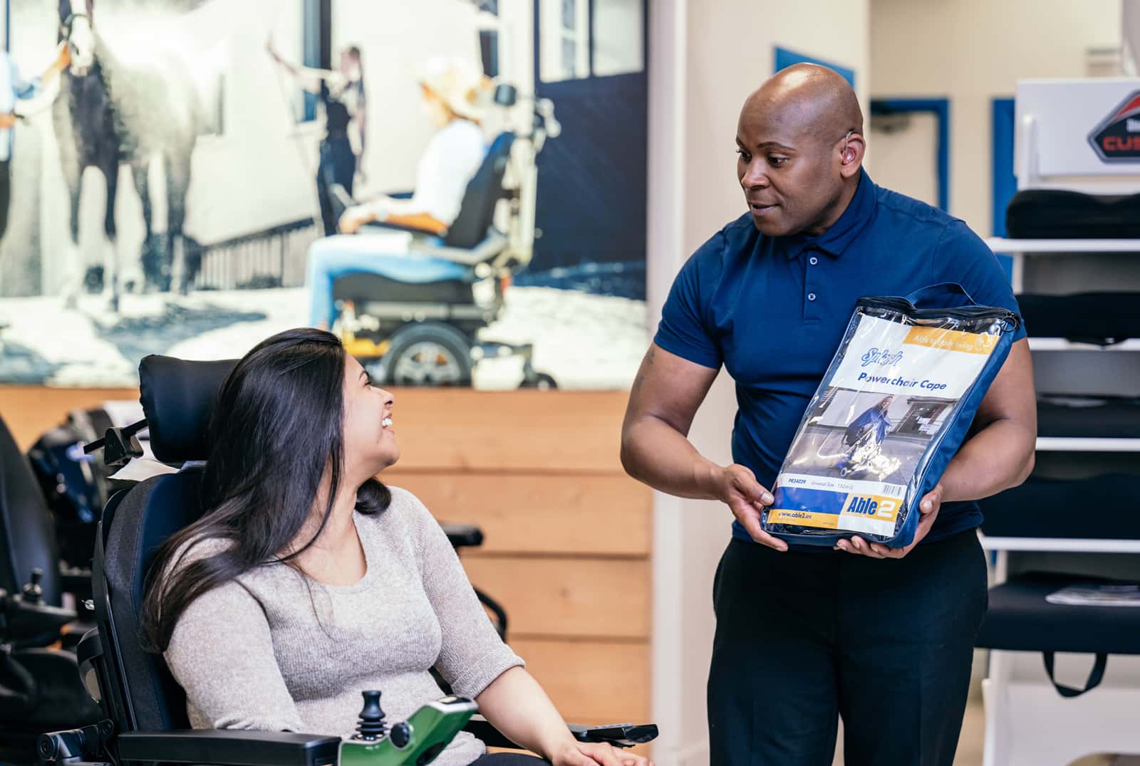 A dealer is stood presenting an information booklet to a powered wheelchair user. The powered wheelchair user is sat in their chair looking back at the dealer.