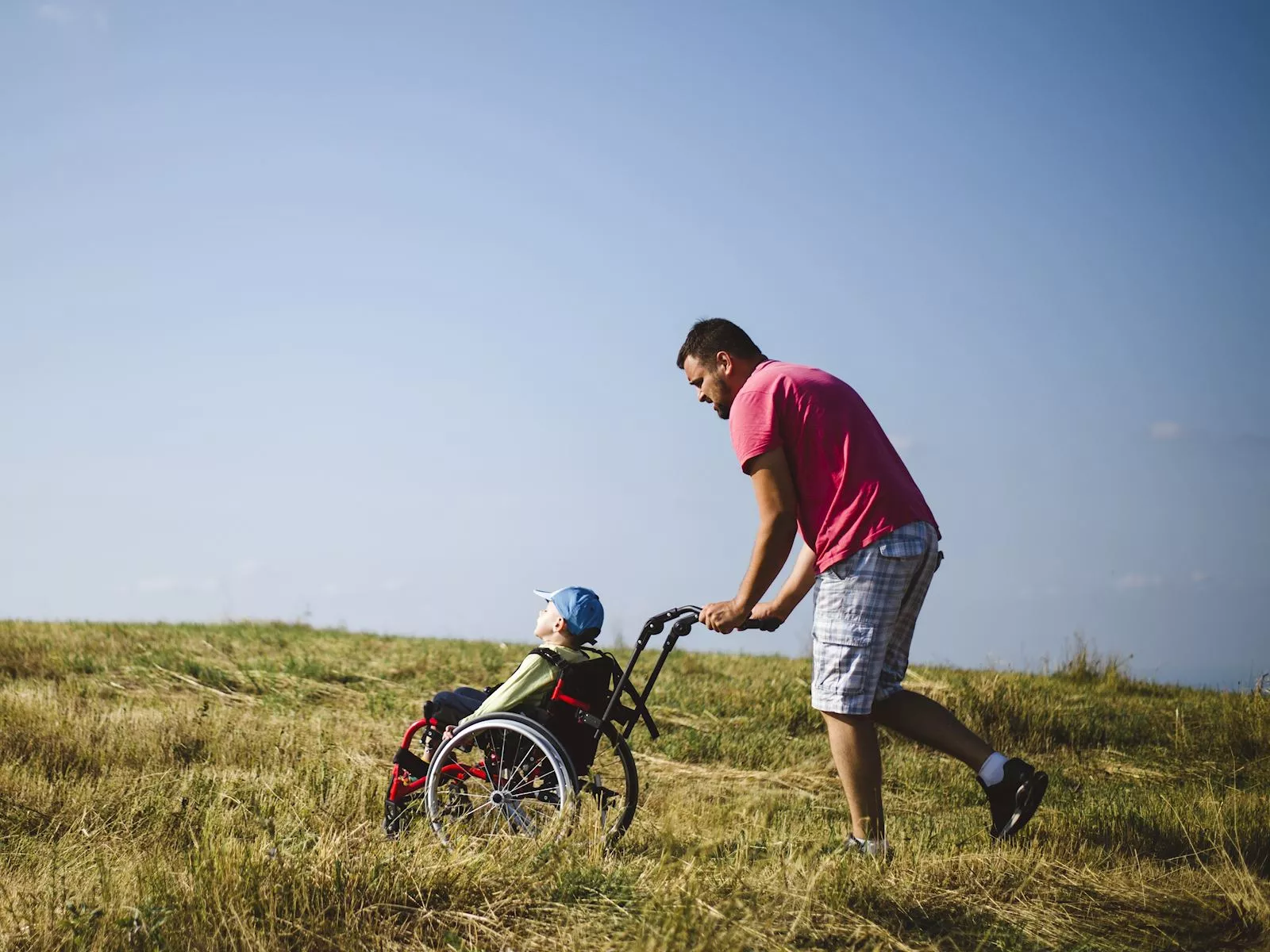 Man pushing child on wheelchair in a field