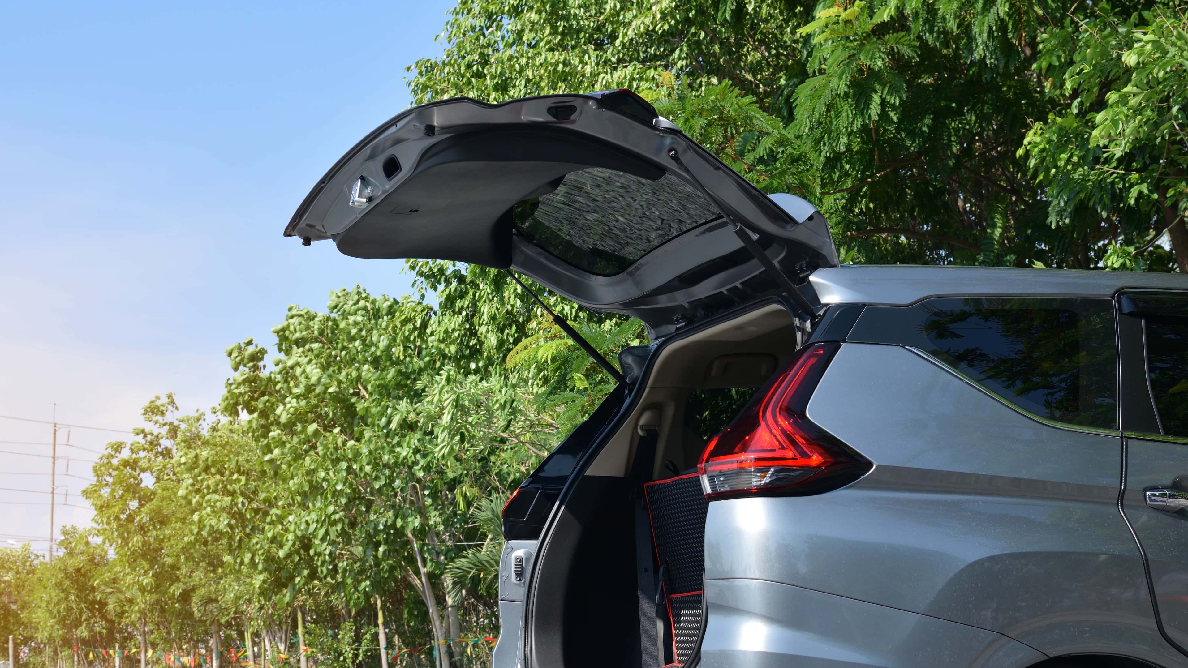 Open boot of a silver car parked outdoors, with sunlight filtering through surrounding green trees.