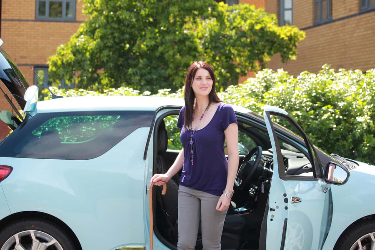 Woman with walking stick getting out of a car