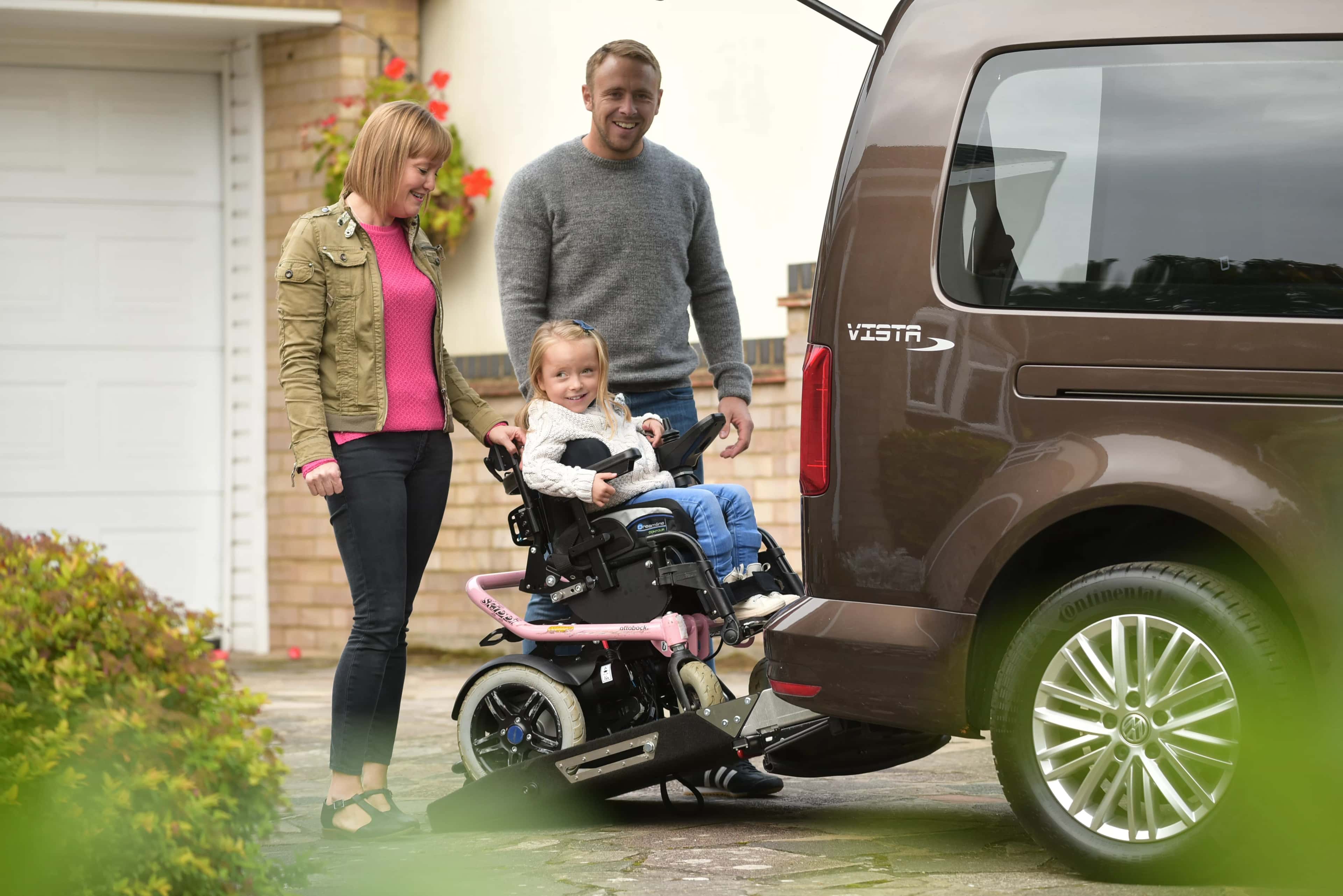 A family helping a little girl in a wheelchair use a rear ramp on a WAV